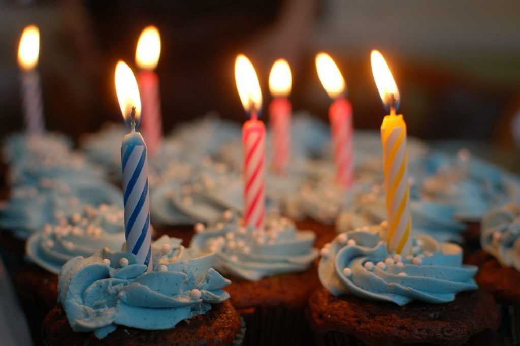 A imagem apresenta vários cupcakes com velas de aniversário acesas em cada um dos bolinhos.